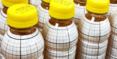 várias garrafas de plástico com tampa amarela e manga termo retrátil branca com linhas pretas